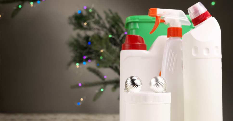 Produtos de limpeza posicionados à frente de uma árvore de Natal iluminada sugerem a dedetização para festa de fim de ano.