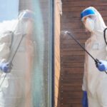 Técnico de macacão e protetor facial aplica produto na fachada para dedetização no frio.